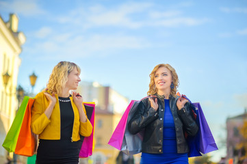 two girls go and smile down the street with shopping bags in their hands