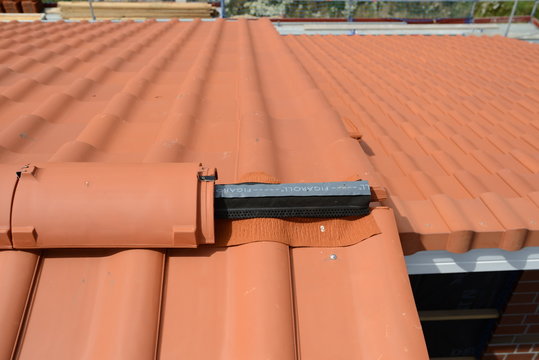 Dachdecken mit Tradition im Handwerk: Dachdecker Bauarbeiten mit Dachziegel auf dem Bau, letzter First auf dem Dach
