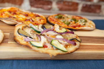 three pizzas on a wooden board, fresh out of the oven. Focus on vegetable pizza