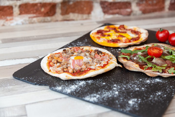 three pizzas on a black board garnish with flour and two tomato