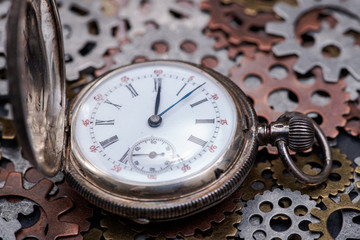 Antique pocket watch and old vintage hour metallic gears on natural stone background.