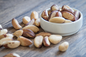 White bowl with Brazil nuts and wooden background.