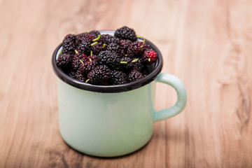 Fototapeta na wymiar Blackberry with leaves. Ripe blackberries in a bowl on a wooden board on a dark background