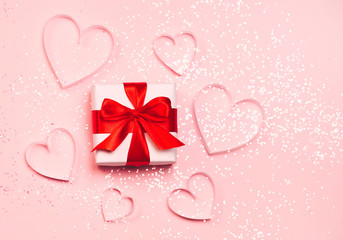 Gift box and paper hearts with sparkling glitter on pink background. Romantic Valentine's day concept of greetings. Top view, flat lay.