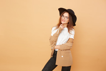 Beautiful stylish brunette girl with long hair in glasses and a black hat on her head dressed in...