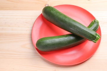 Fresh zucchini on a red plate and wooden background. Healthy food.