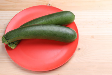 Fresh zucchini on a red plate and wooden background. Healthy food.