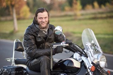 Young bearded happy smiling motorcyclist in black leather clothing sitting on shiny modern powerful...