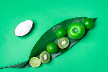 Green fruits on a leaf on green table. Above view. Healthy eating.