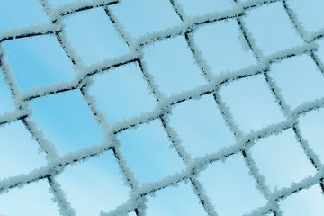 hoarfrost on steel wire mesh in winter against blue sky, close-up
