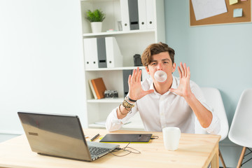 Business, fun and joke concept - young man blowing bubble of chewing gum in office