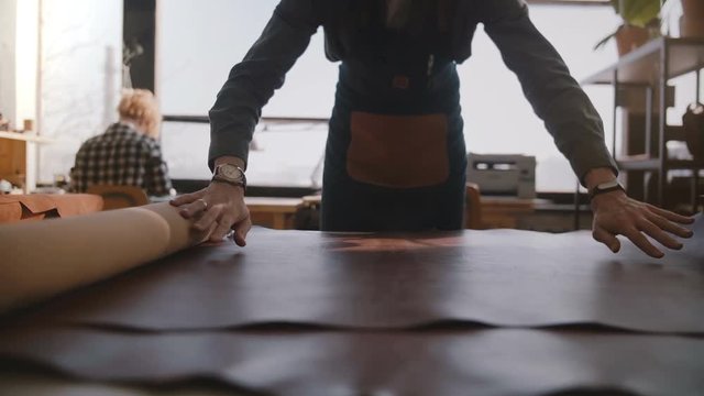 Close-up view of professional craftsman spreading a big piece of leather in modern manufacturing workshop slow motion.