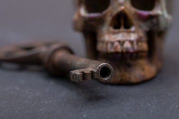 Old antique vintage metallic key and stone carved skull on natural stone background.
