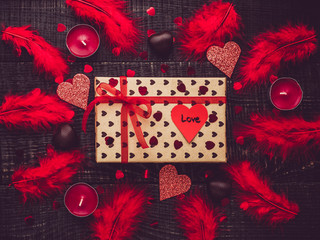 Colorful gift box and paper heart with words of love on the background of dark surface, feathers and motley confetti. Flat lay, close-up. Congratulations for relatives, friends and colleagues