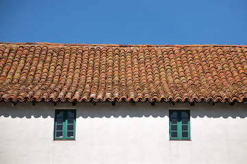 Red tile roof on an old Spanish building, with a blue sky background