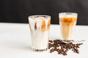 Ice coffee in a glass with cream over and coffee beans on the table