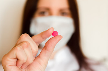 Doctor with a medical mask keeps one pink pill close up
