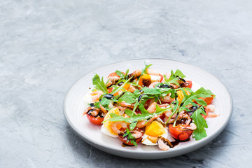 Ready-to-eat salad with cherry tomatoes, eggs, boiled shrimp, arugula, sesame seeds and balsamic sauce in a plate on the table