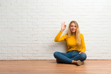 Fototapeta na wymiar Young girl sitting on the floor showing an ok sign with fingers