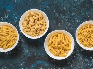 Various dry pasta in white plates on a blue grunge background. Top view. Copy space