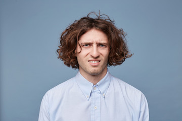 The guy with an untidy messy hairstyle looks camera, dressed in an ordinary light shirt, a facial...