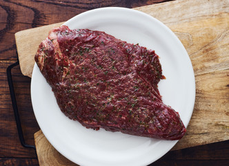 Raw marinated steak with various spices on a wooden board top view