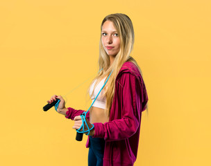 Pretty sport woman with jumping rope on yellow background