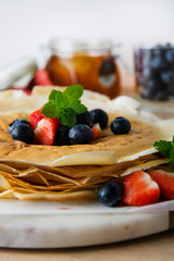 Rolled up crepes, pancakes on a plate with blueberries and strawberries.
