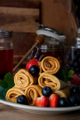 Rolled up crepes, pancakes on a plate with blueberries and strawberries. Vertical image.