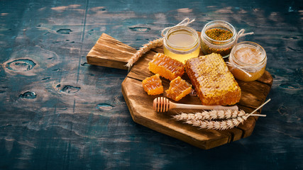 A set of honey and bee products. Honey in honeycomb. On a black wooden background. Free space for text. Top view. - obrazy, fototapety, plakaty