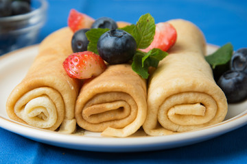 Rolled up crepes, pancakes on a plate with blueberries and strawberries. Vertical image.