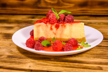 White plate with cheesecake New York, leaves of mint and raspberries on wooden table