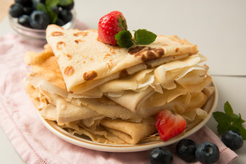Homemade pancakes on a plate with blueberries and strawberries.