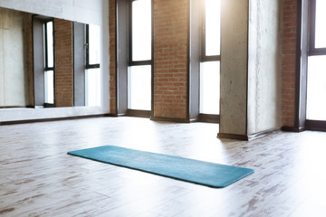 Gym loft interior with blue yoga mat, big windows and sunlight, no people. Copy space