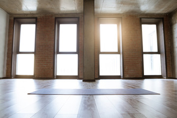 Gym loft interior of fitness studio with blue yoga mat, big windows and sunlight, no people. Copy...