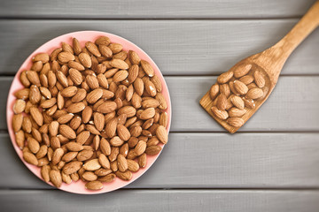 Almond nuts in a pink plate on a gray wooden surface. Healthy food