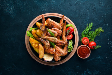 Baked chicken wings with potatoes and vegetables on a black background. Meat. Top view. Free copy space.