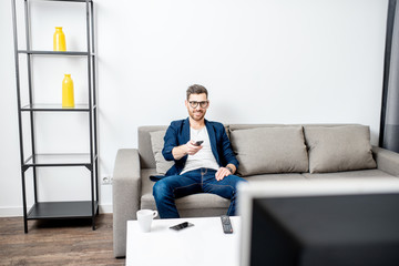 Handsome businessman dressed casually watching TV on the couch at home