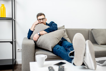 Cute man dressed casually relaxing on the couch with a pillow while watching TV at home