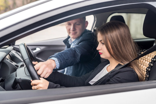 Instructor helping young woman drive a car