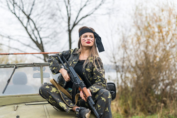 Woman in military uniform with rifle and car