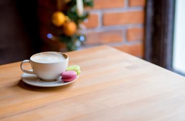 Colorful macaroons and coffee cup on window background