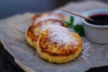 Fried cheesecakes or pancakes on craft paper on stone plate with blueberry jam.