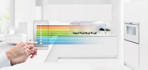energy saving and smart home automation control concept hand touch screen of cell phone with efficiency class symbol on blurred kitchen background