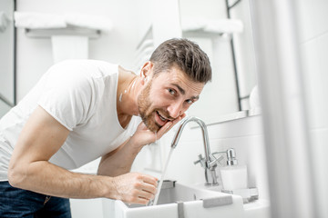 Man washing his face with fresh water and foam in the sink at the white bathroom
