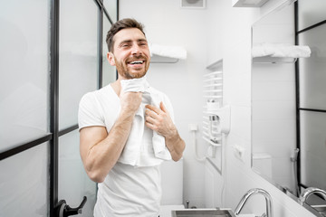 Naklejka na ściany i meble Portrait of a handsome man in white t-shirt drying his face with towel in the bathroom