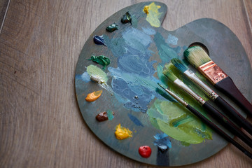 Artist palette with oil paints and brushes on a wooden background.