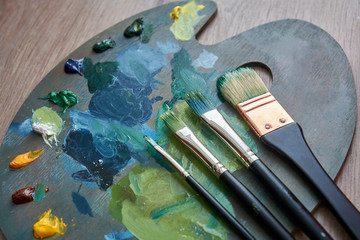 Artist palette with oil paints and brushes on a wooden background.