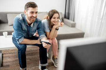 Young lovely couple with happy emotions watching TV sitting together on the table at home