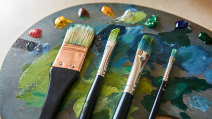 Artist palette with oil paints and brushes on a wooden background.